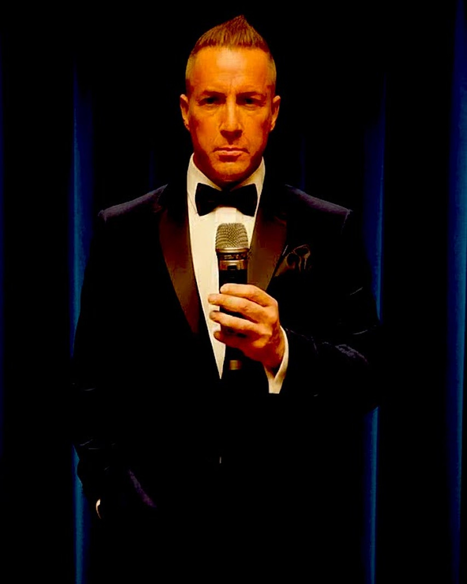 Barry Shaw in a velvet tuxedo, holding a microphone
