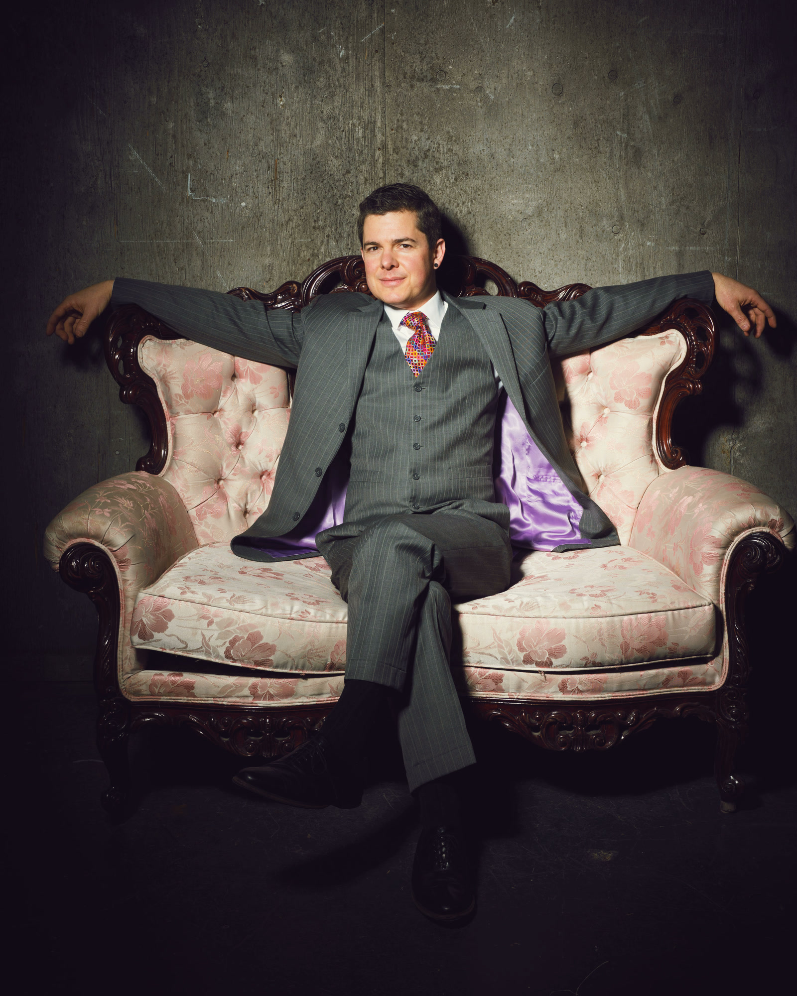 A magician in a three-piece suit seated on a vintage sofa