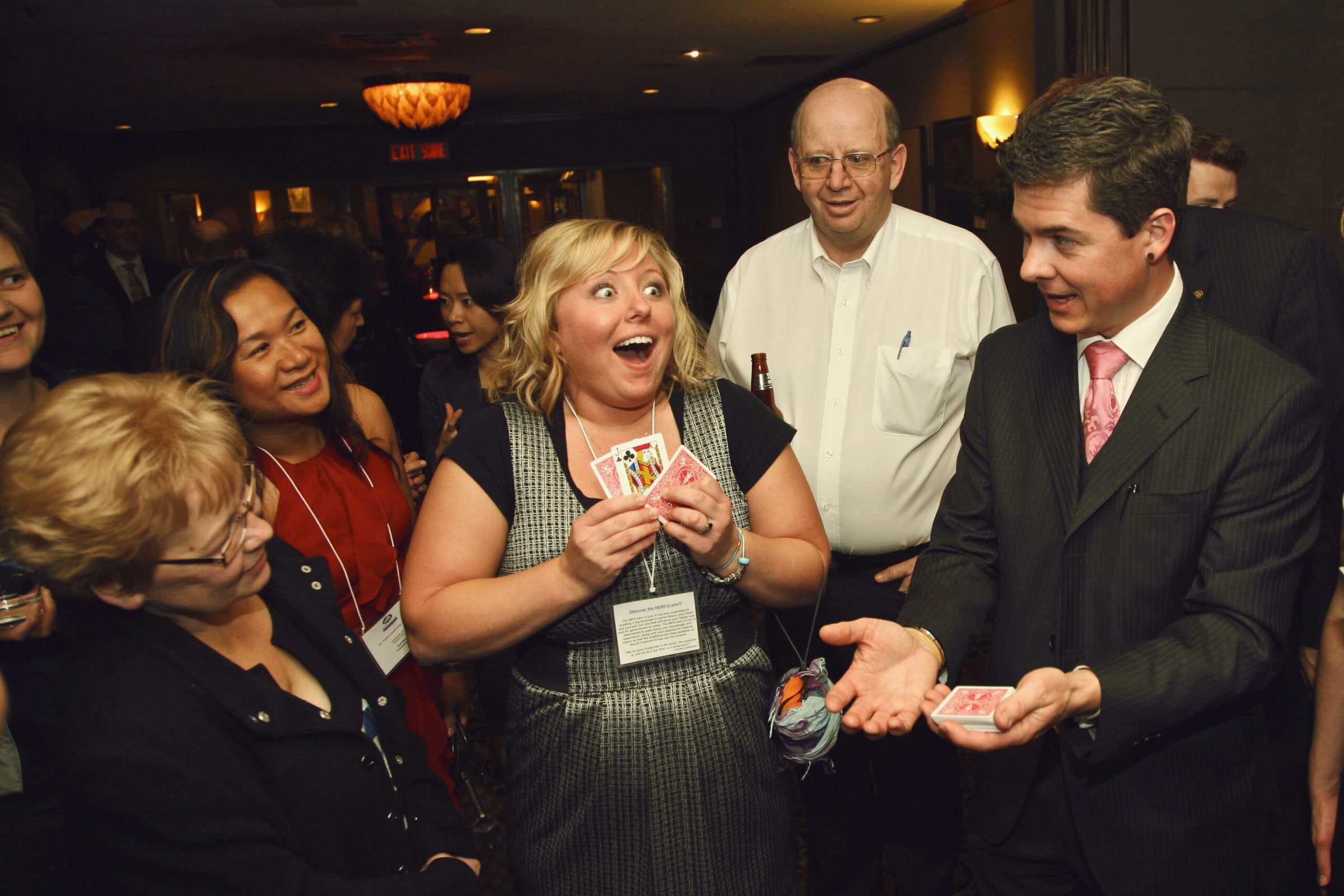 A magician showing a card trick to a group of guests as one of them gasps
