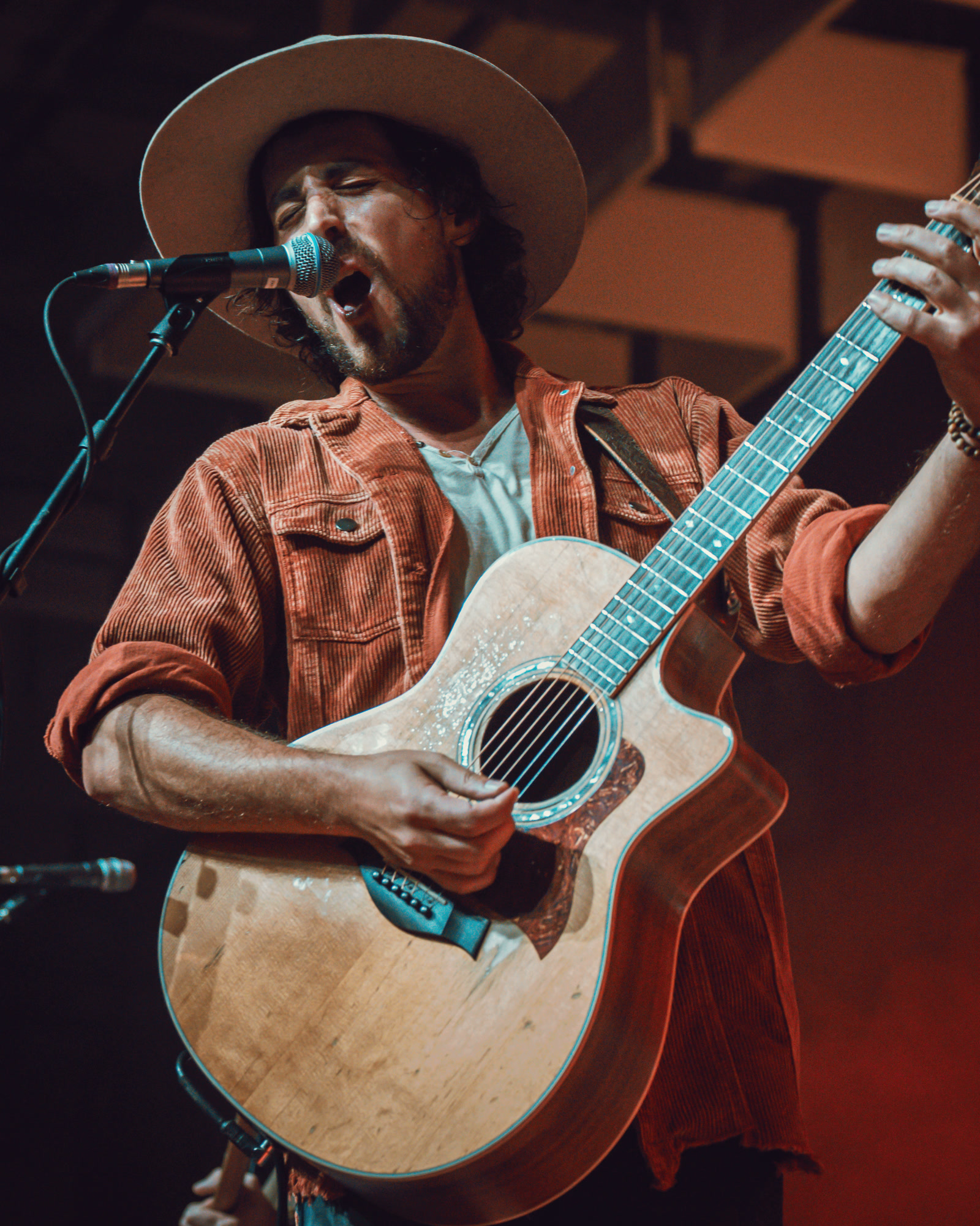 A singer in a brimmed hat at the microphone, playing an acoustic guitar