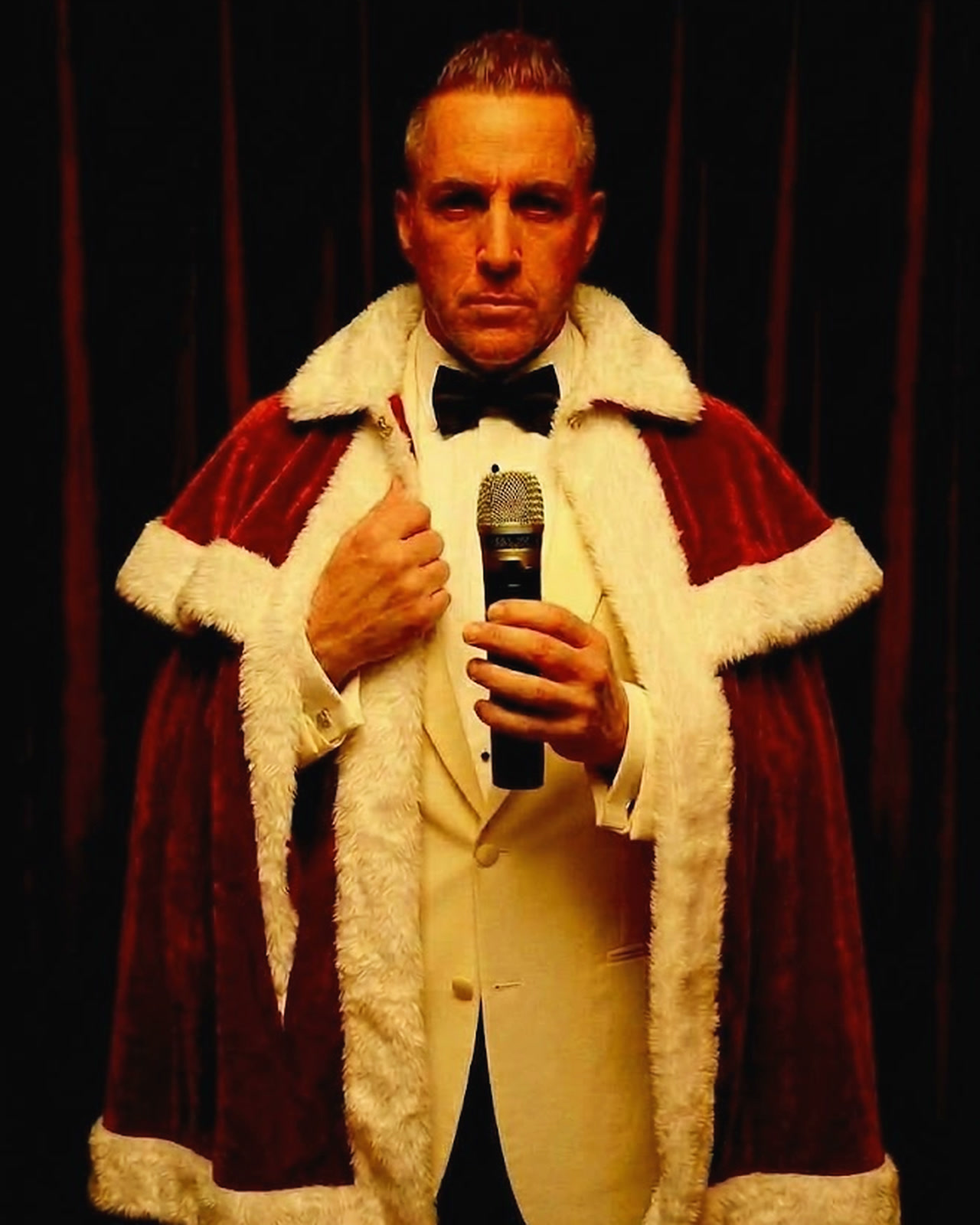 Barry Shaw in a cream tuxedo and a red holiday robe, holding a microphone
