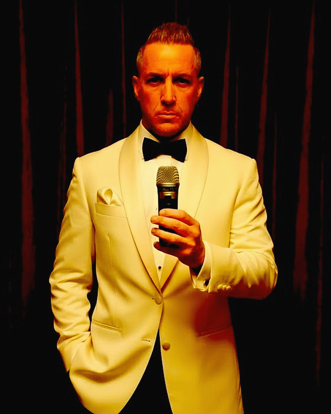 Barry Shaw in a cream tuxedo and black bow tie, holding a microphone