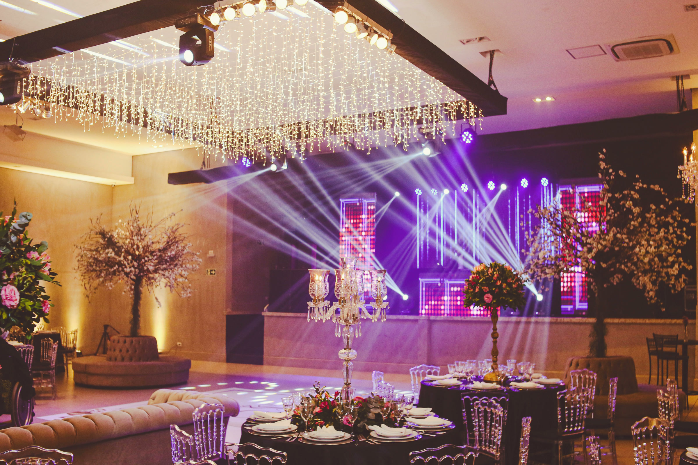 An empty banquet hall set for a party, with the stage lights on and tables laid